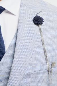 Uomo che indossa un abito grigio chiaro con cravatta blu navy e spilla a forma di fiore su sfondo bianco