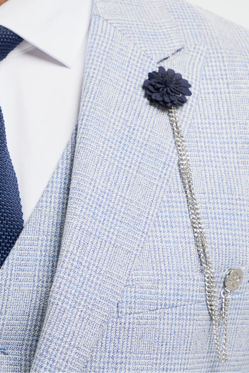 Uomo che indossa un abito grigio chiaro con cravatta blu navy e spilla a forma di fiore su sfondo bianco