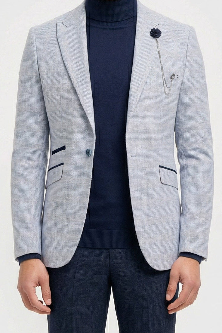 Uomo che indossa un blazer grigio chiaro, un dolcevita blu navy e pantaloni scuri su uno sfondo bianco