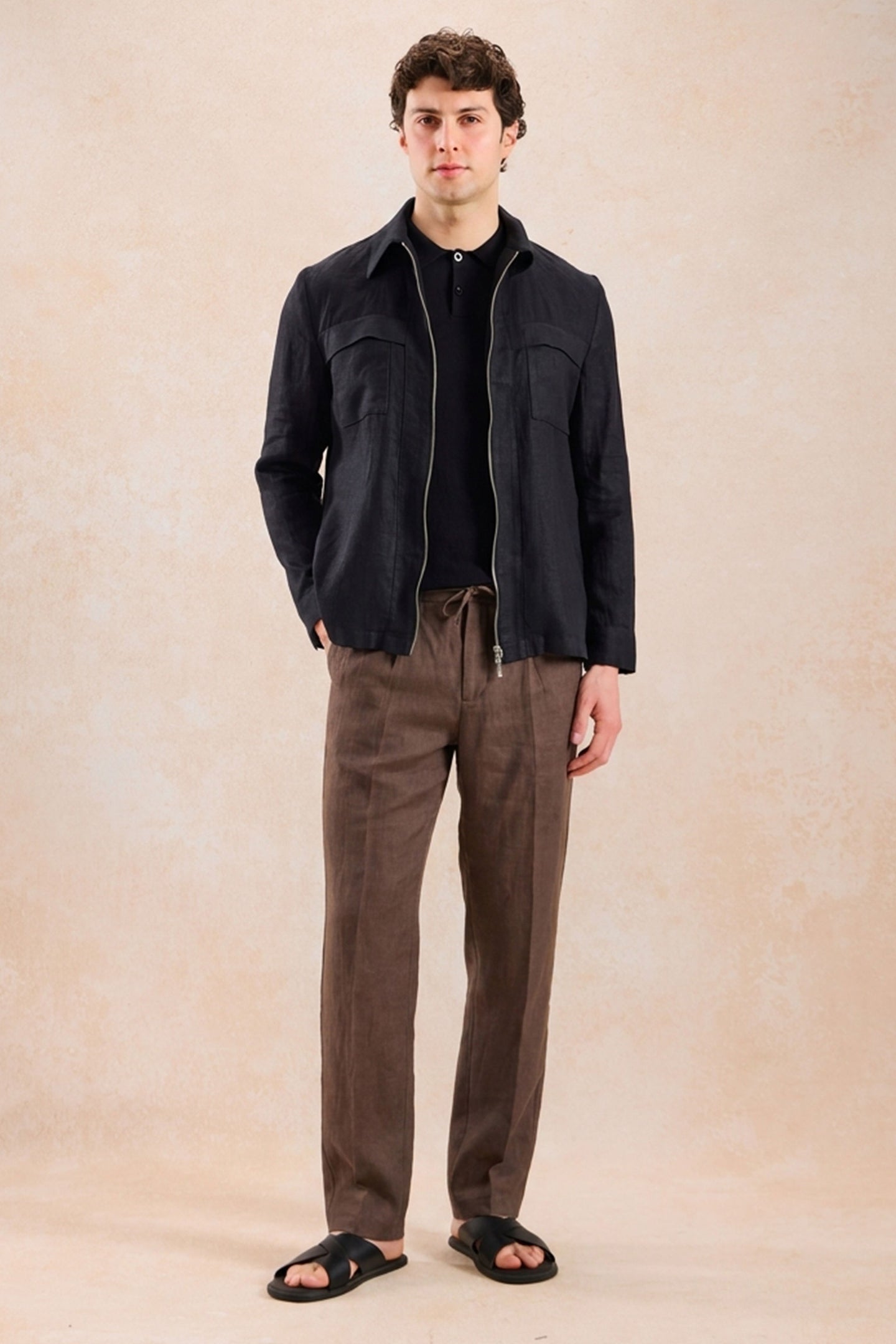 Completo estivo da uomo composto da giacca nera con zip in lino e pantaloni marroni, elegante e casual.