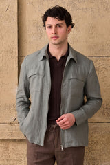 Completo estivo da uomo composto da giacca in lino verde salvia con zip e pantaloni marroni, elegante e casual.
